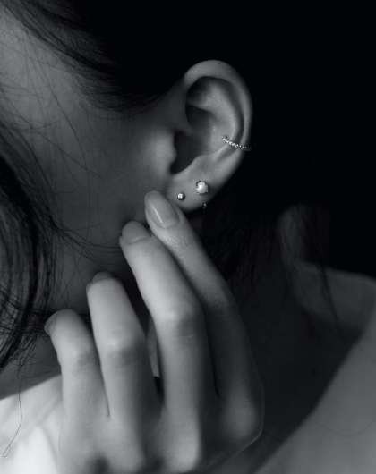 black and white close up of woman's hand touching her ear with multiple stud earrings