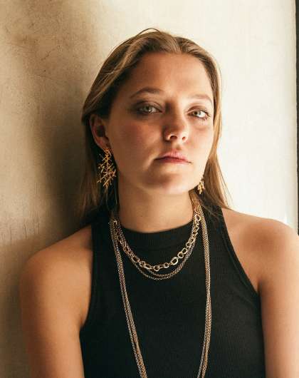 head shot of young woman wearing gold necklaces and intricate dangling earrings